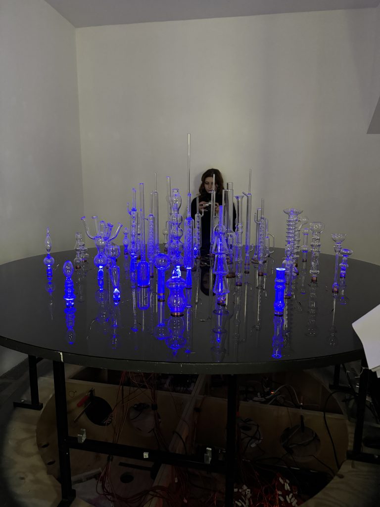 Ein Tisch, auf dem mehrere Glasgefäße unterschiedlicher Formen stehen, die alle blau leuchten. 