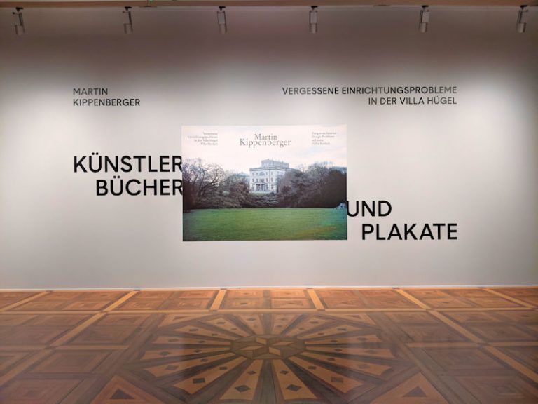 Eingang zur Ausstellung Künstlerbücher und Plakate von Martin Kippenberger in der Villa Hügel. Schriftzug und ein Foto mit der Villa Hügel