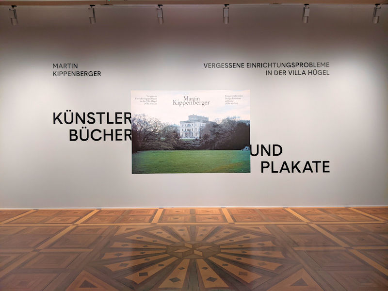 Eingang zur Ausstellung Künstlerbücher und Plakate von Martin Kippenberger in der Villa Hügel. Schriftzug und ein Foto mit der Villa Hügel